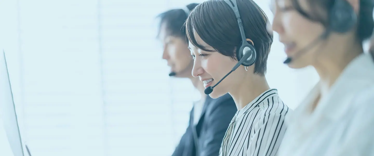 ヘッドセットを付けたコールセンターの女性スタッフがパソコン対応中、「お問い合わせ」の文字入り