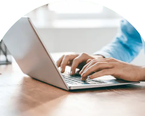 木製のデスクでノートパソコンを操作する人物の手元、作業中の様子を示す