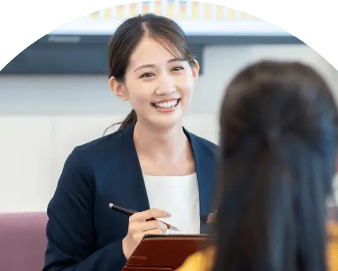 笑顔の女性がペンとタブレットを持ち、目の前の相手と会話している打ち合わせの様子