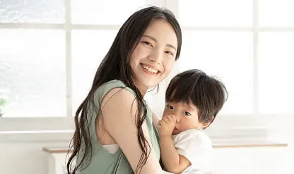 小さな子どもを抱きかかえて微笑む女性。自然光が差し込む明るい室内で撮影
